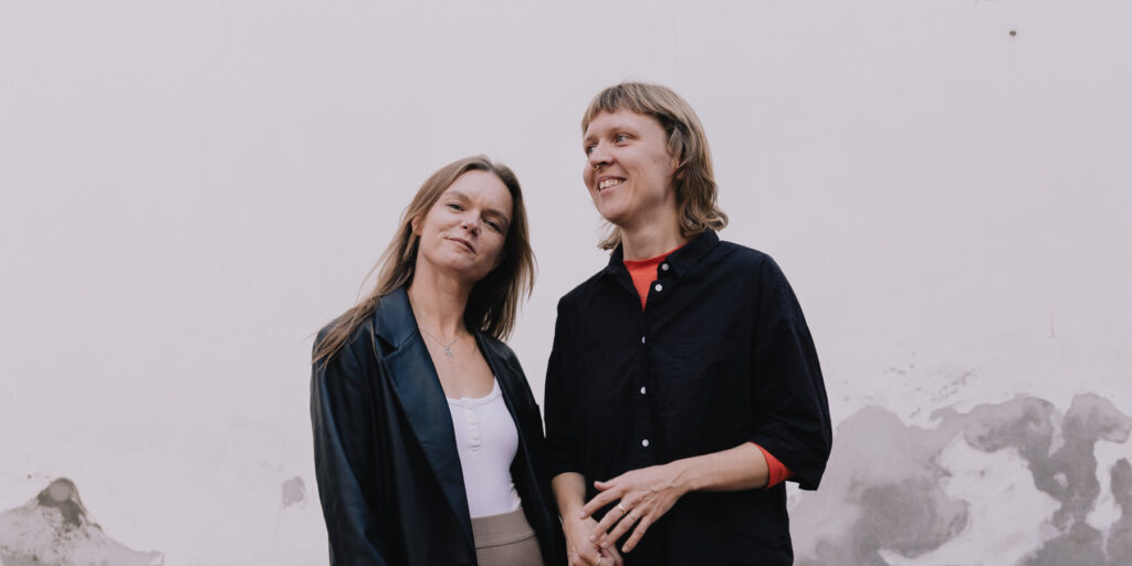 Two people standing together in front of a white wall